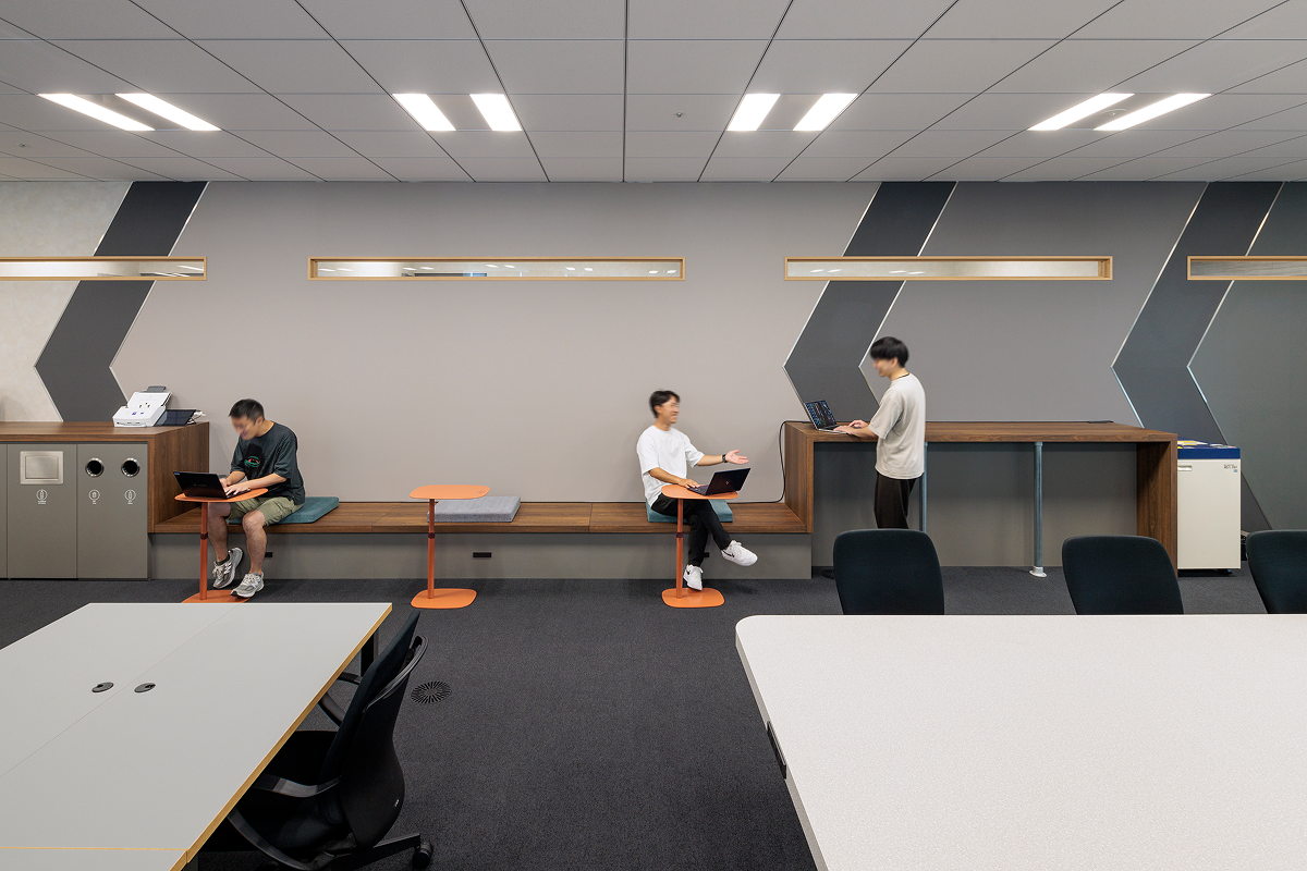 写真：壁際に座席とカウンターが並ぶワークスペース。中央には大きいテーブルと椅子が配置されている。