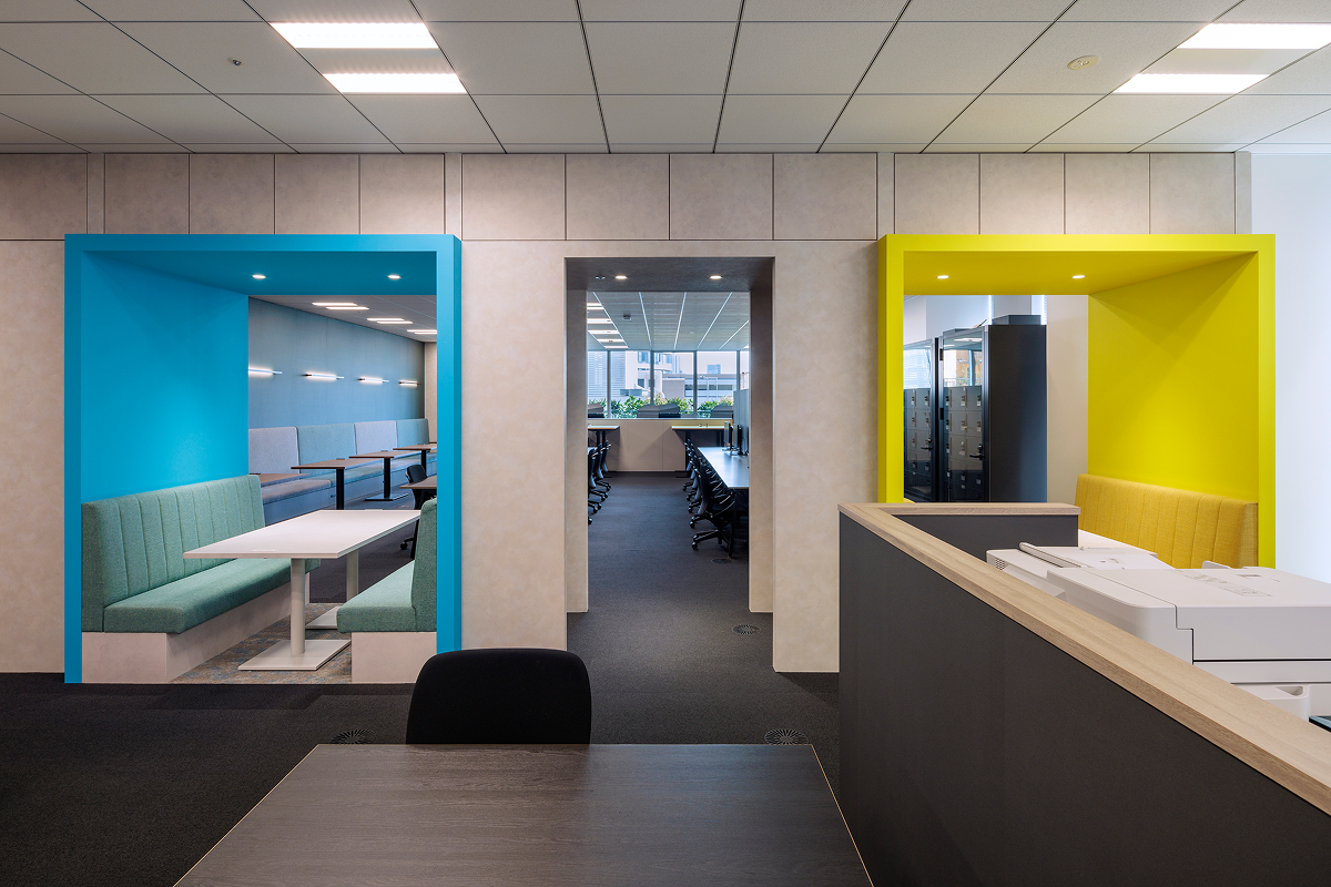 写真：青色と黄色のボックス席が2つと、中央奥にデスク席が並ぶ開放的な空間。