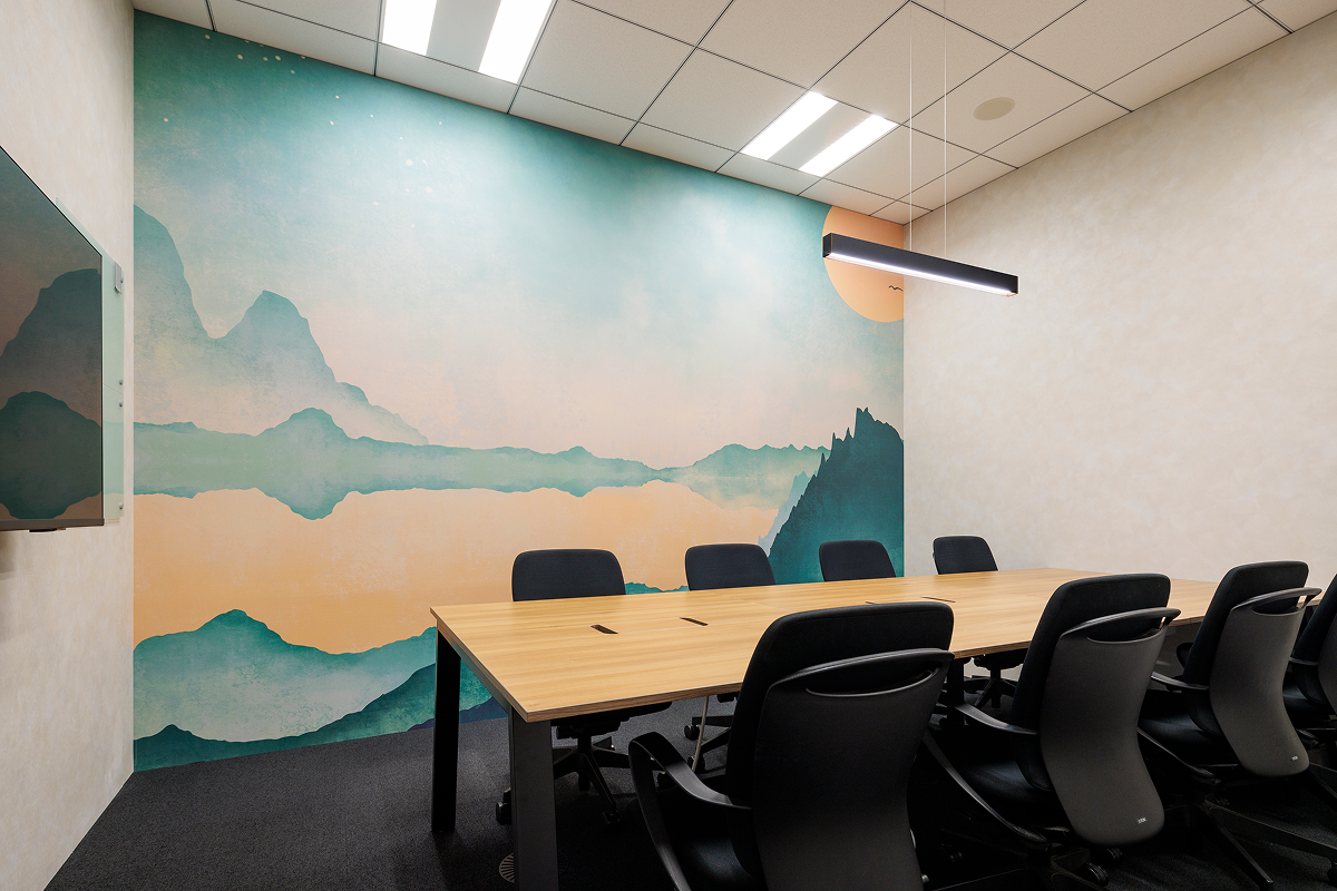 写真：壁に風景画が描かれた会議室。長いテーブルと黒い椅子が並ぶ。